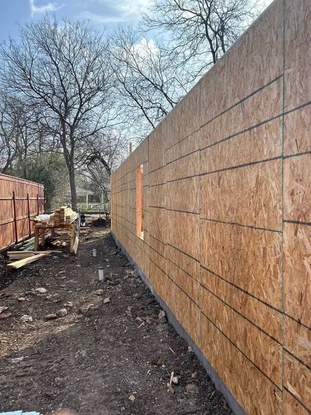 Narrow dirt path between plywood construction walls under bare trees on a cloudy day