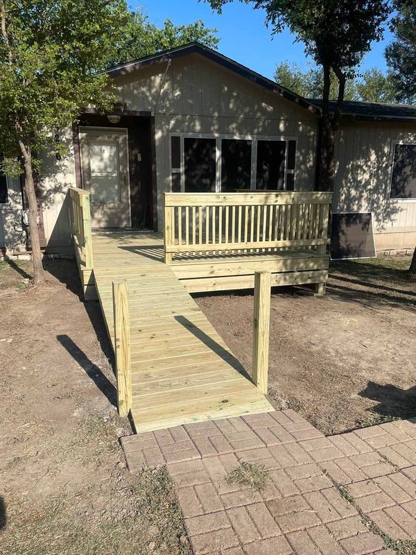 Accessible wooden ramp leading to a small building entrance with a porch and railing