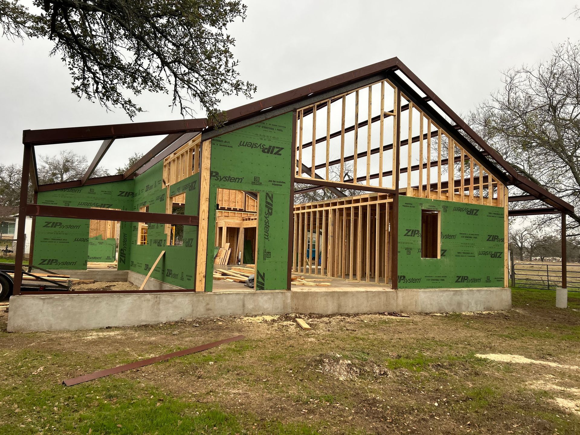 Partially framed green house under construction on a concrete foundation, with exposed roof trusses and open windows.