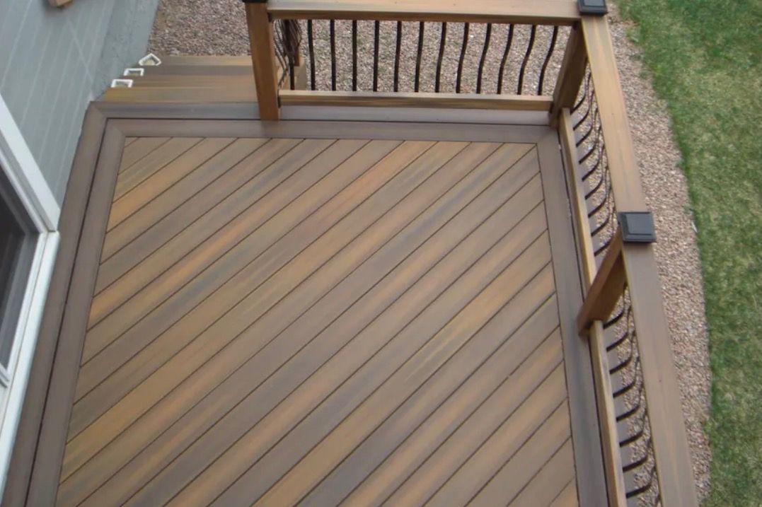 Wooden deck stairs and landing with diagonal plank flooring beside a gravel path and lawn