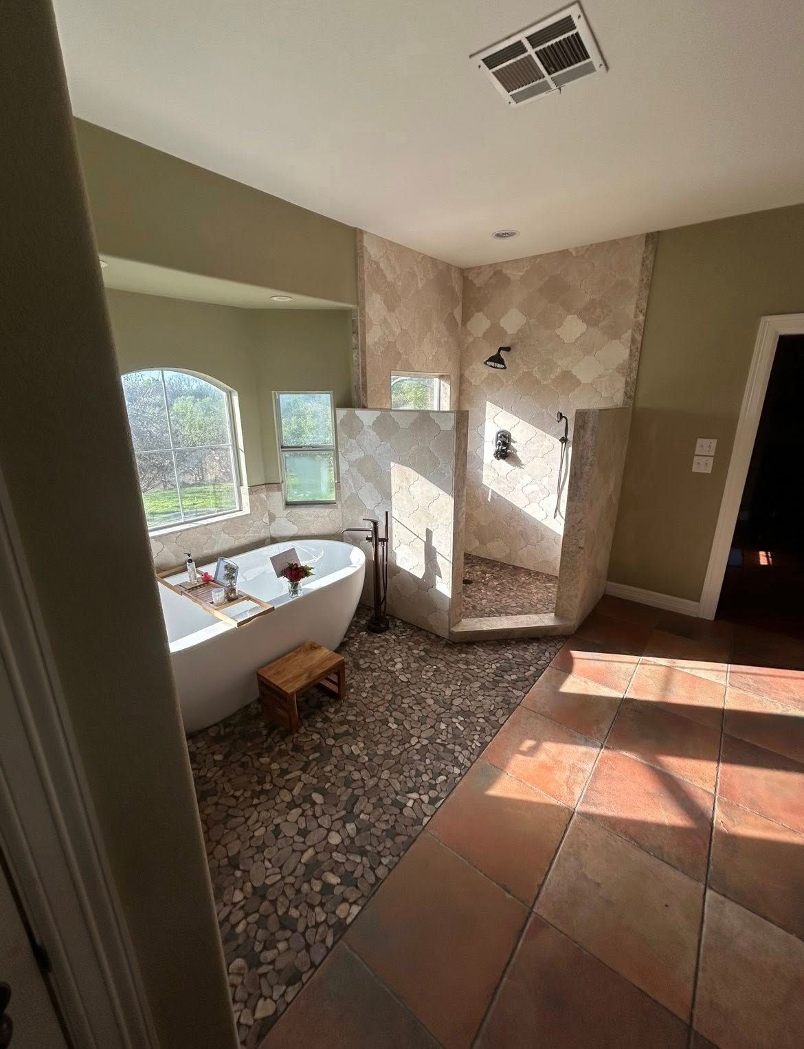 Bathroom with freestanding tub, tiled shower, and terracotta floor in warm natural light