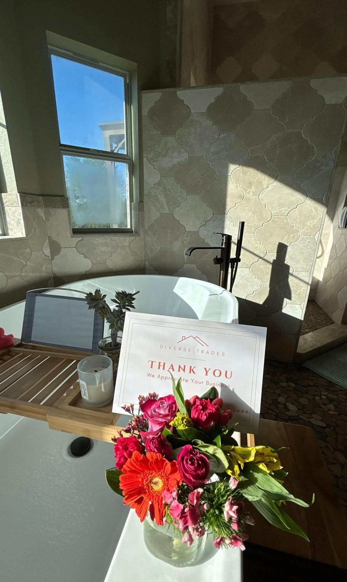 Thank-you card beside a bouquet of pink and orange flowers on a sunlit table by a window