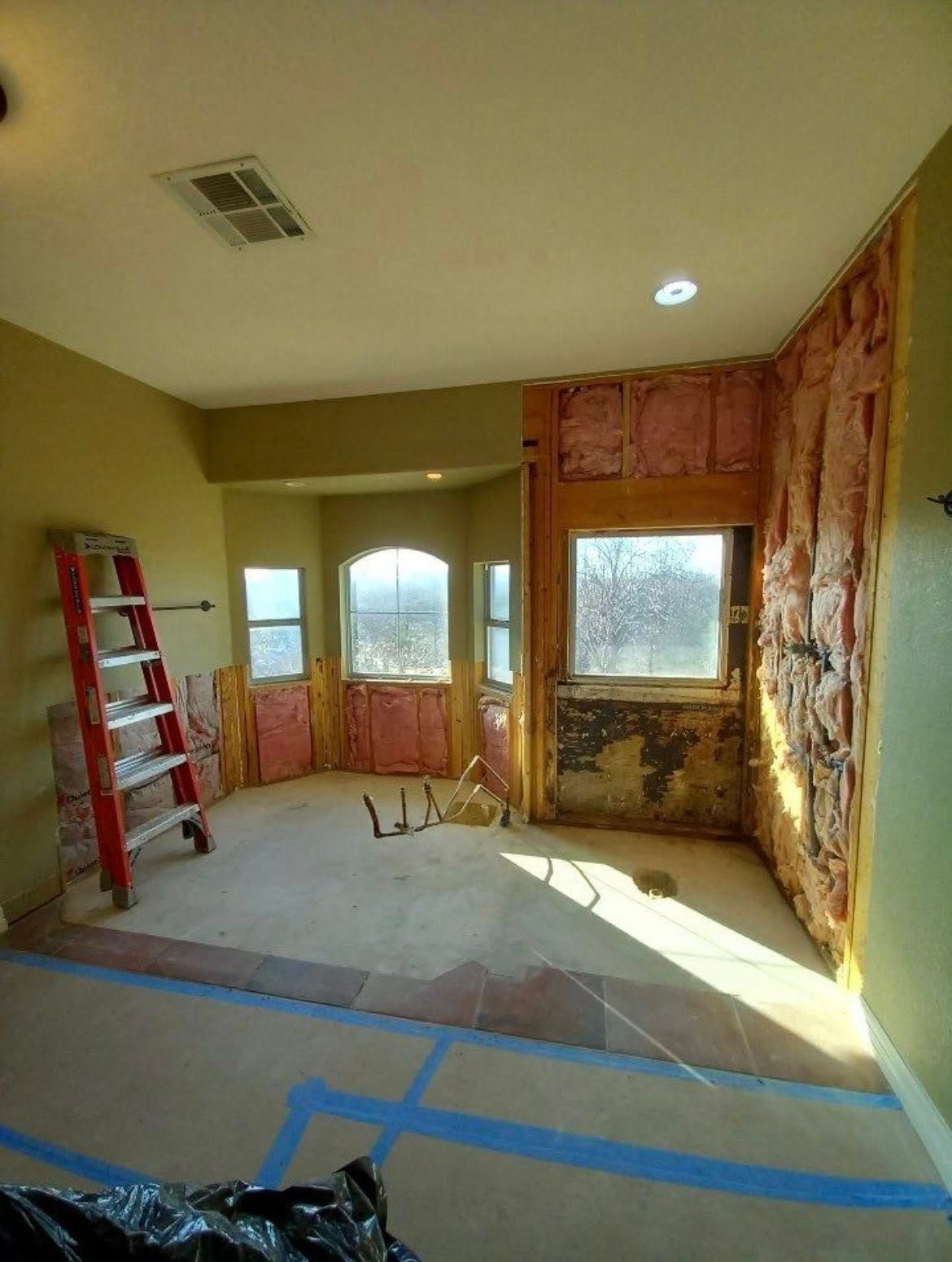 Empty room under renovation with red ladder, taped floor, and sunlight through large windows