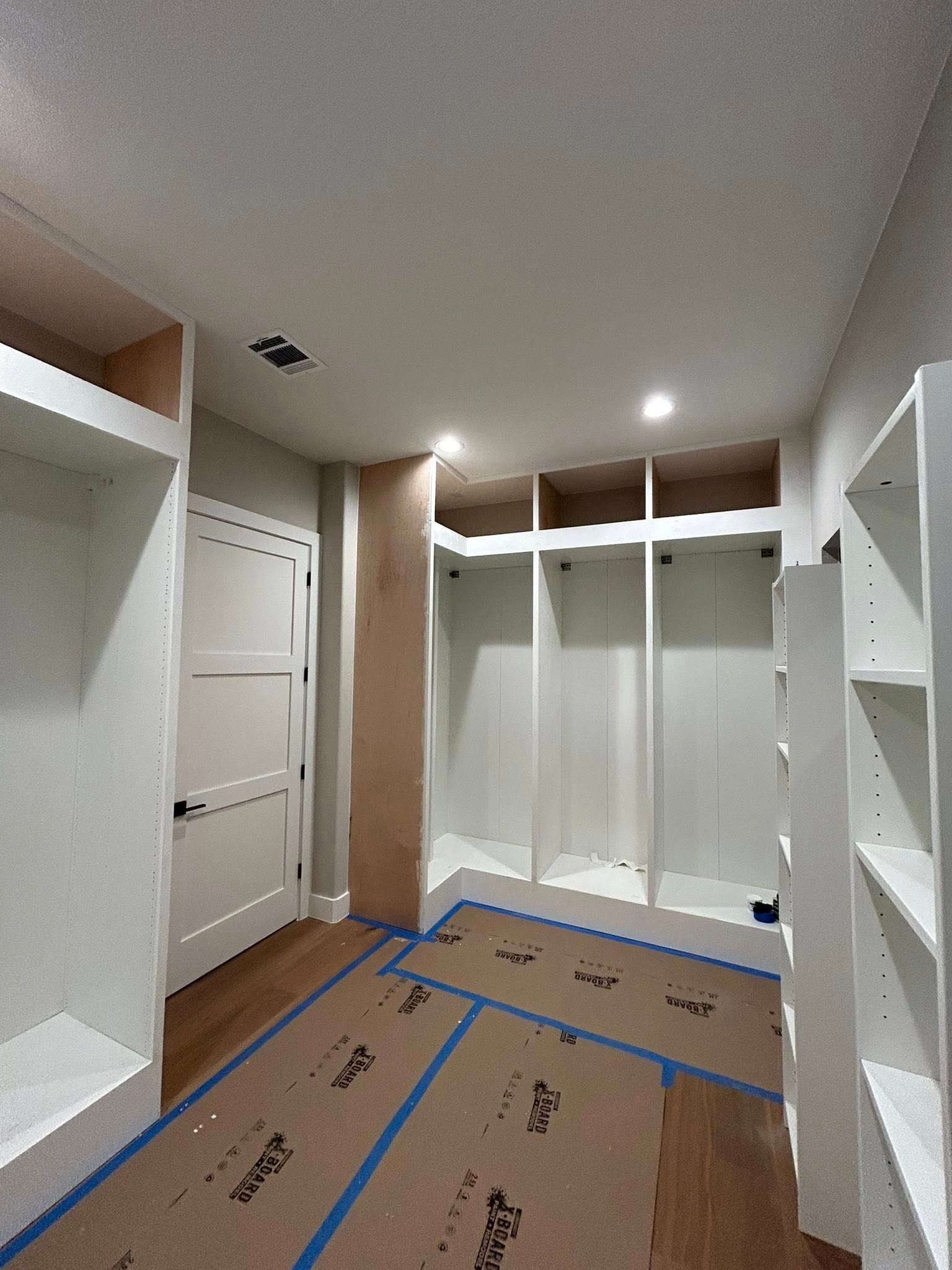 Empty walk-in closet with white shelving, hanging rods, and cardboard-covered floor during installation.