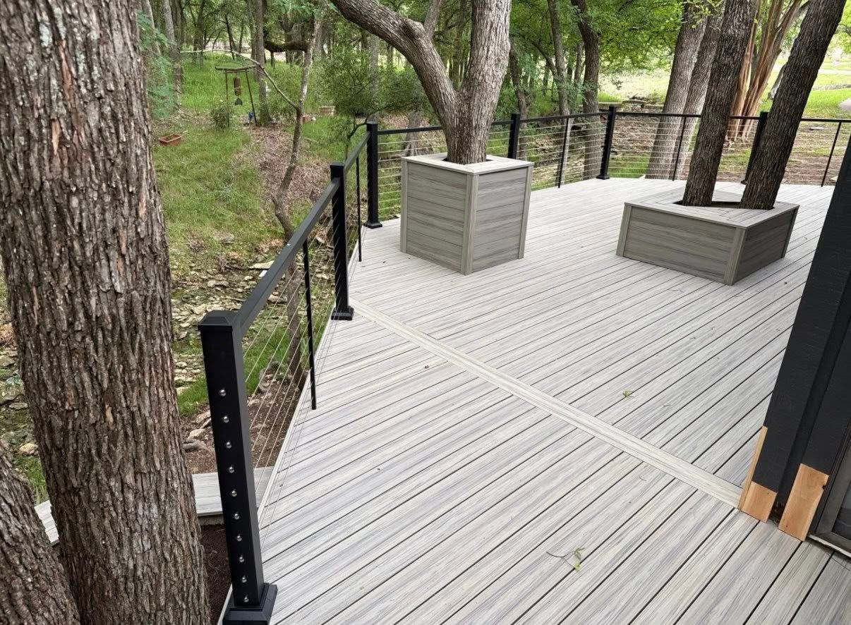 Wooden deck walkway with black railings and rectangular planters among trees in a wooded area