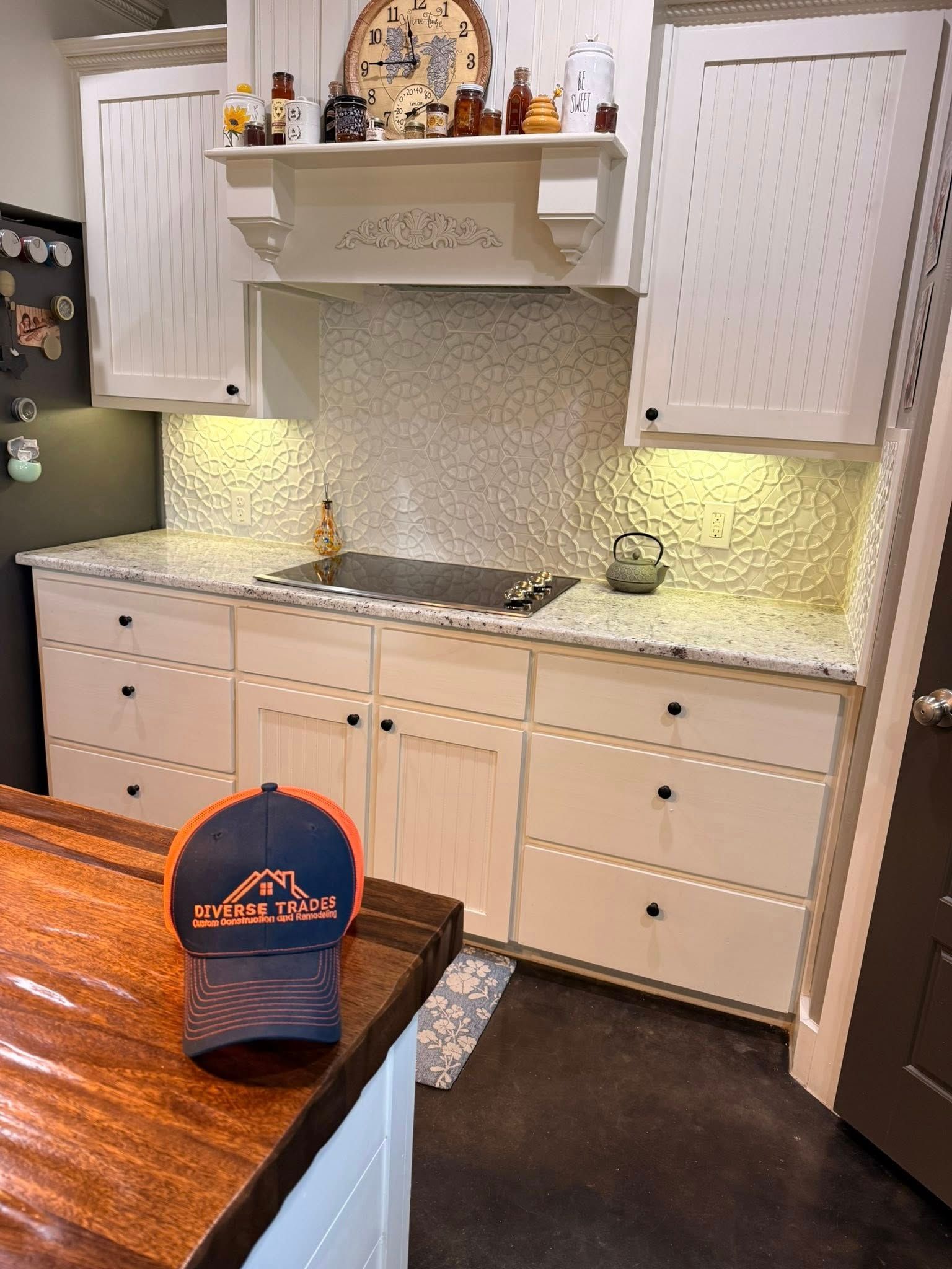 White kitchen with lit cabinets, tiled backsplash, stove, sink, and a blue cap on a wooden table.