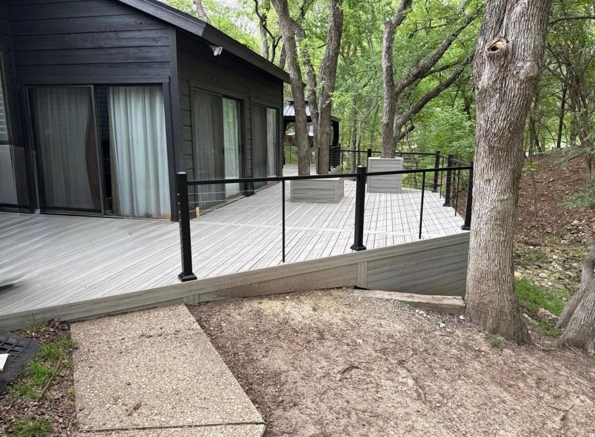 Wooden deck ramp with black railings beside a dark cabin in a wooded area