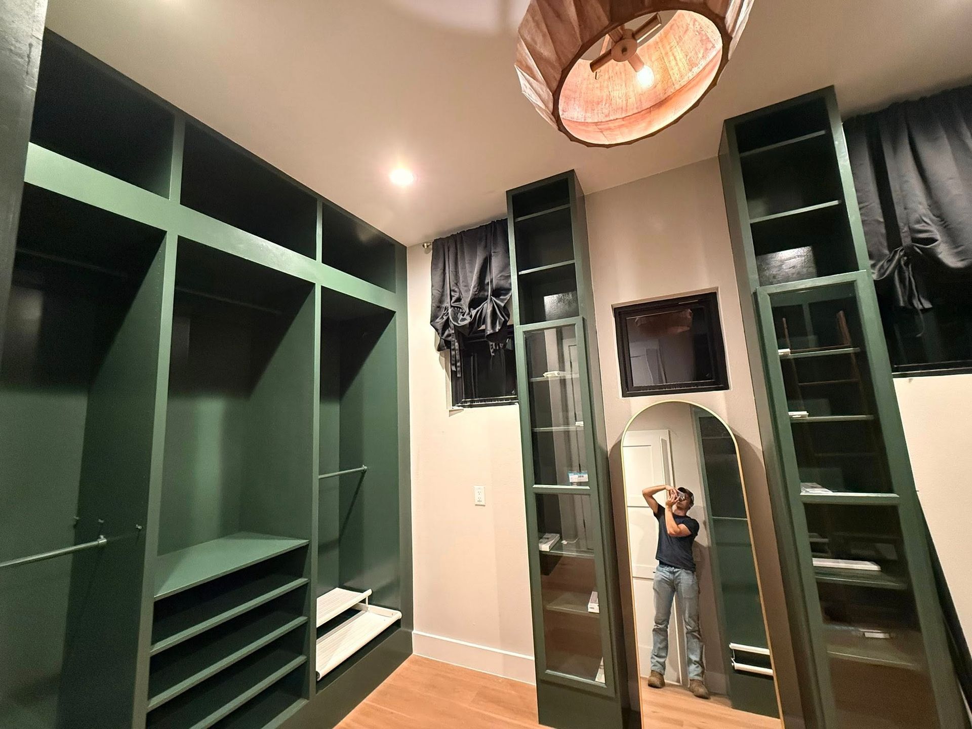 Walk-in closet with dark green shelves, mirrored doors, and a person taking a mirror selfie