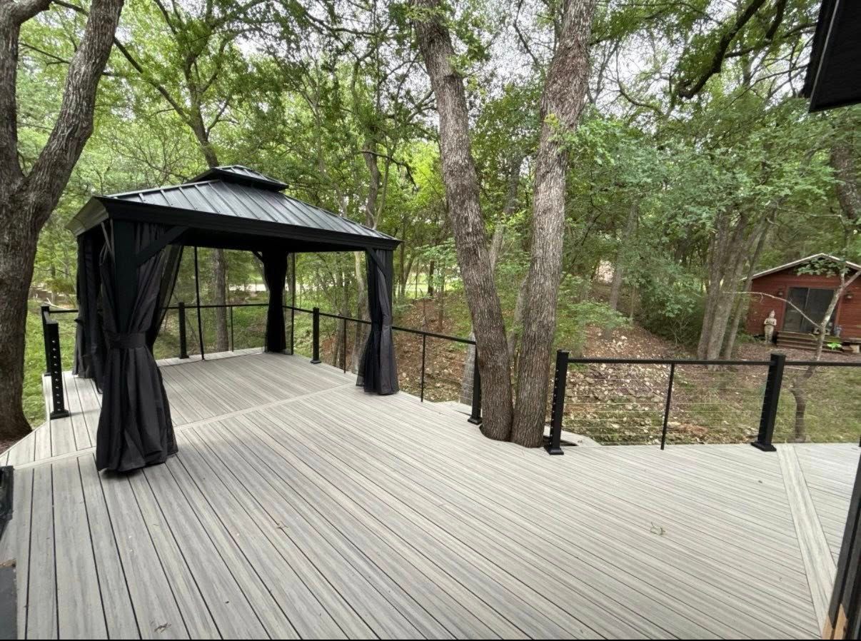 Wooden deck with a black gazebo, surrounded by trees and a railing in a wooded setting