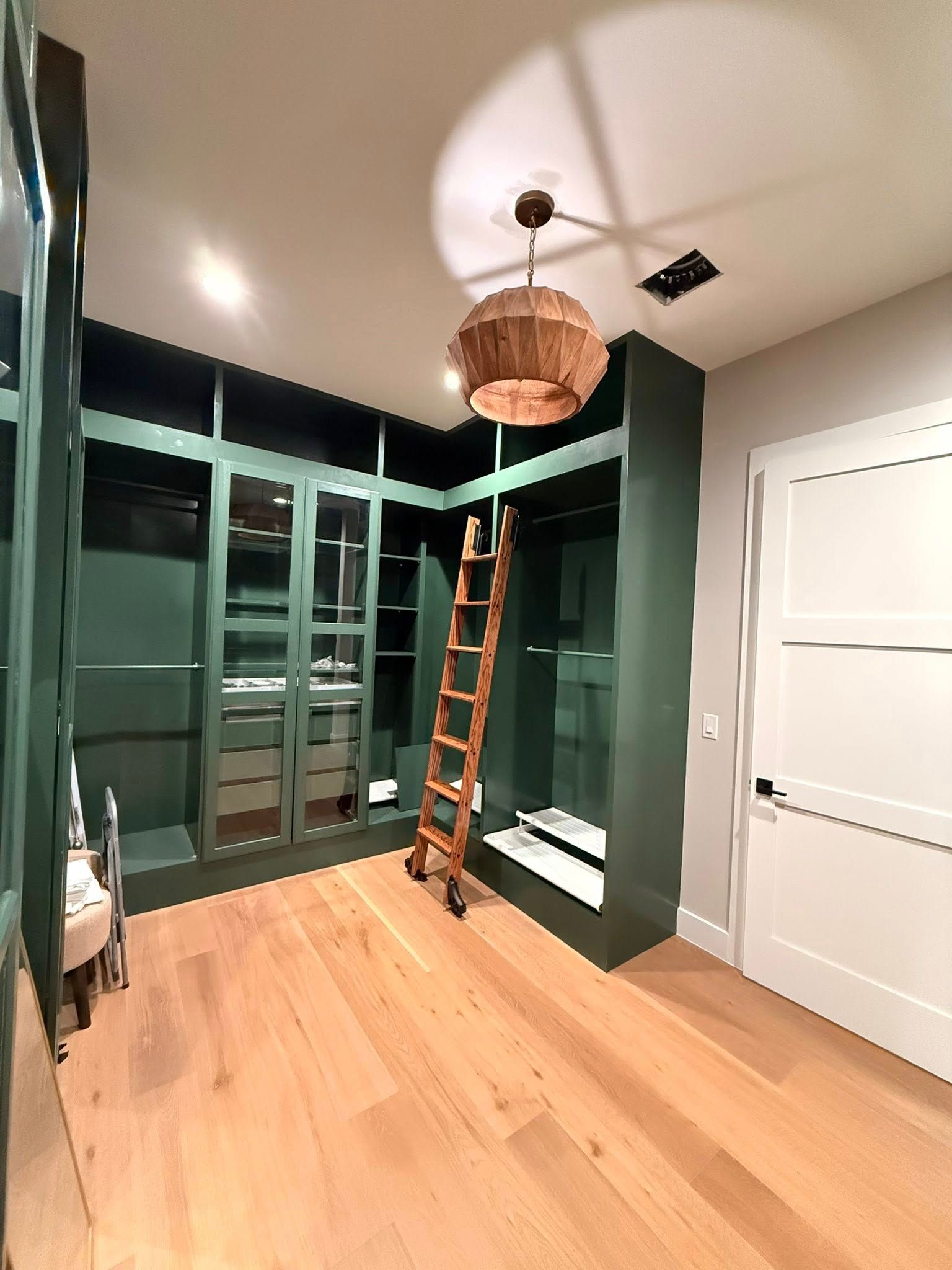 Built-in green closet room with a wood floor, ladder, and woven pendant light chandelier