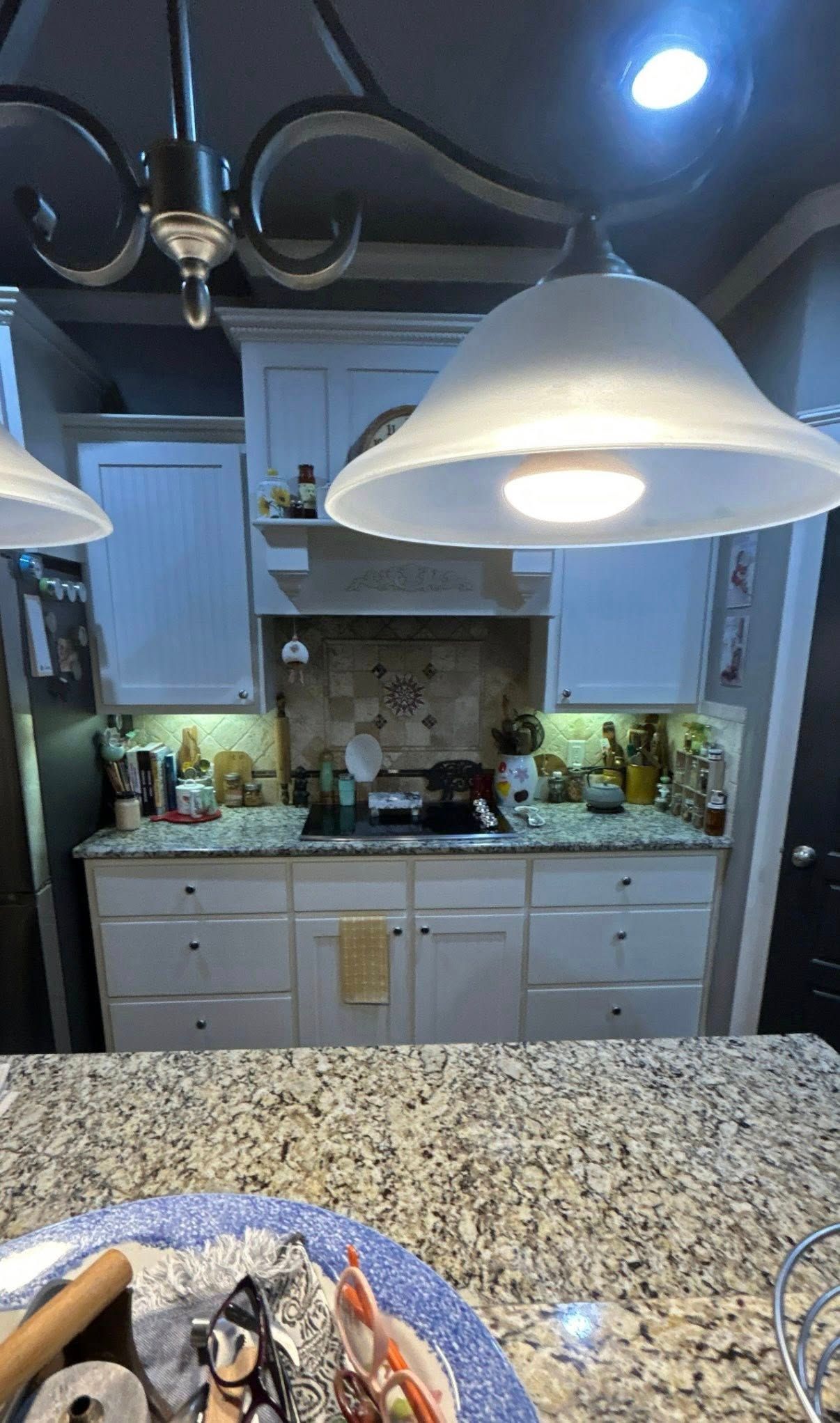 Kitchen viewed from a granite counter, with hanging white pendant lights and cabinets in the background.