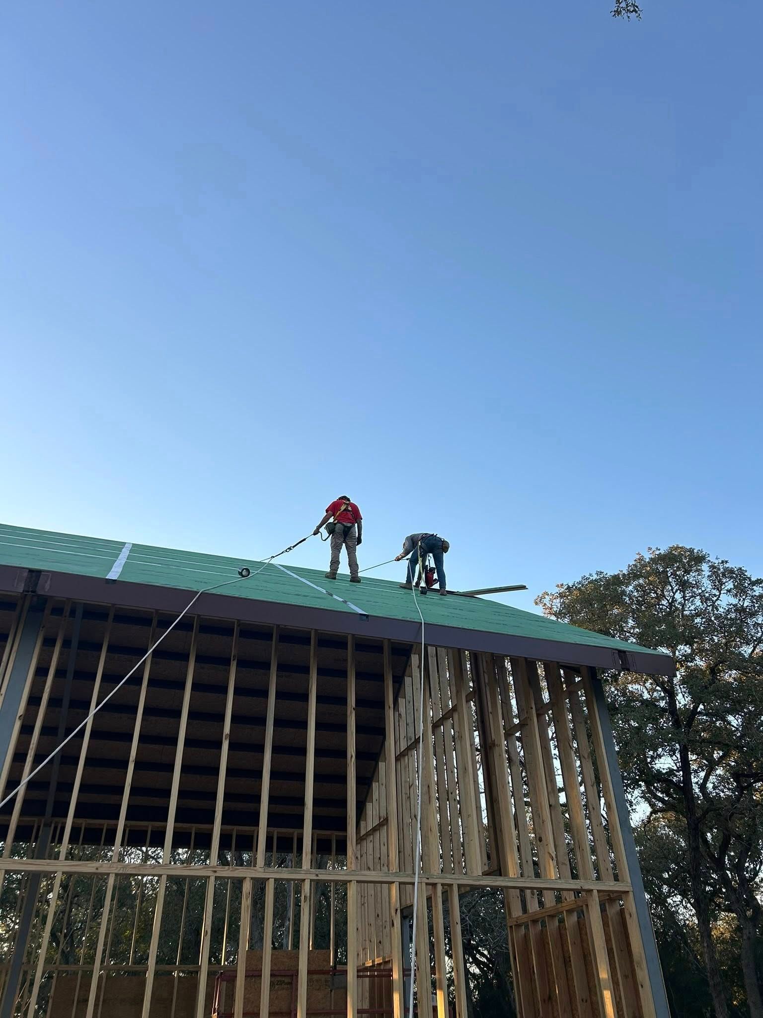 Workers on a roof framing a building under a clear blue sky
