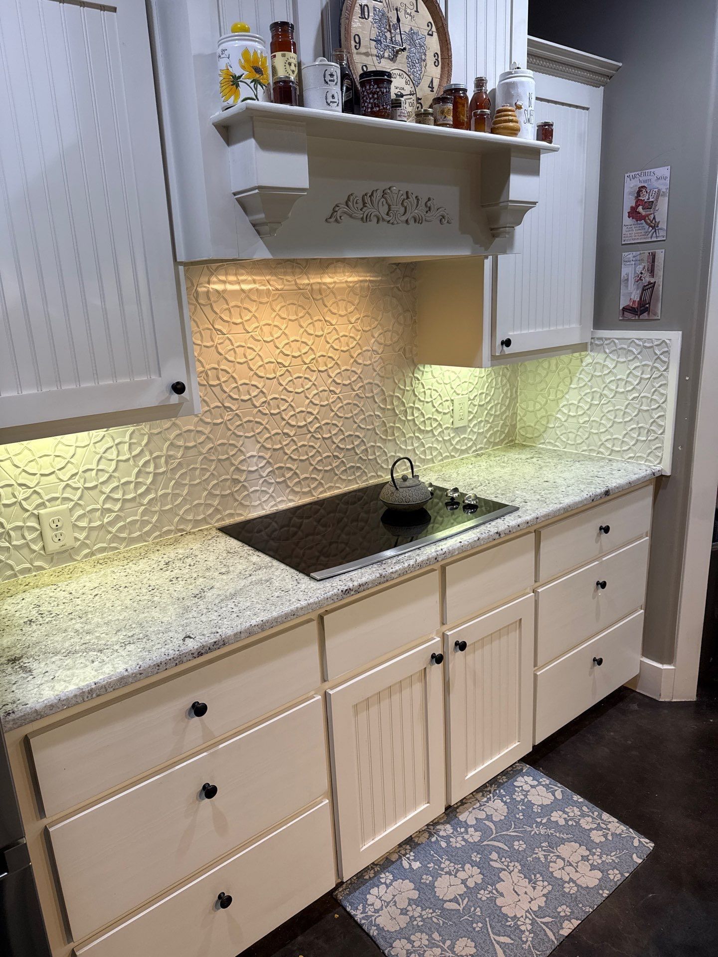 Kitchen counter with under-cabinet lighting, white cabinets, and a black cooktop on a speckled countertop.