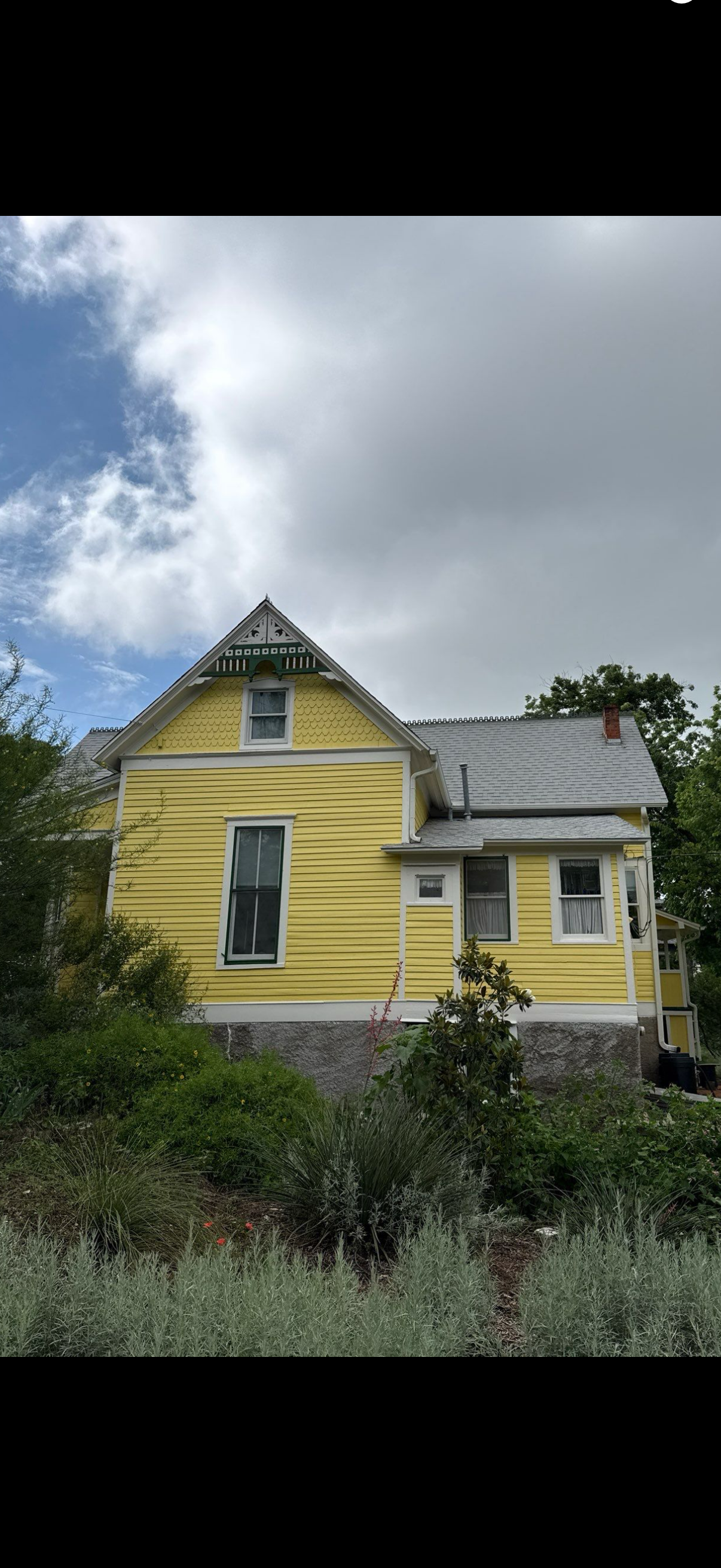 Yellow Victorian-style house with white trim, steep roof, and front porch under a cloudy sky