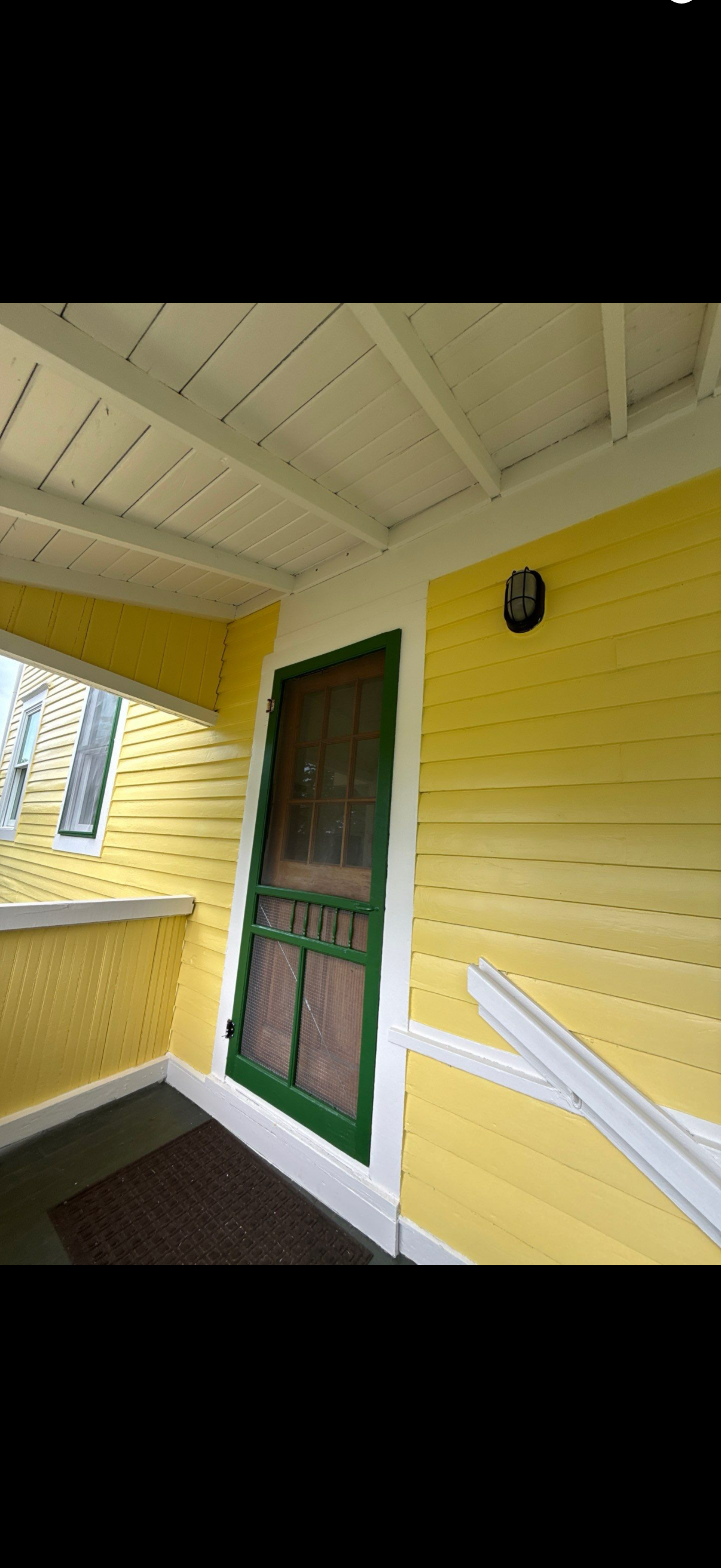 Yellow porch with green door and white trim under a covered ceiling