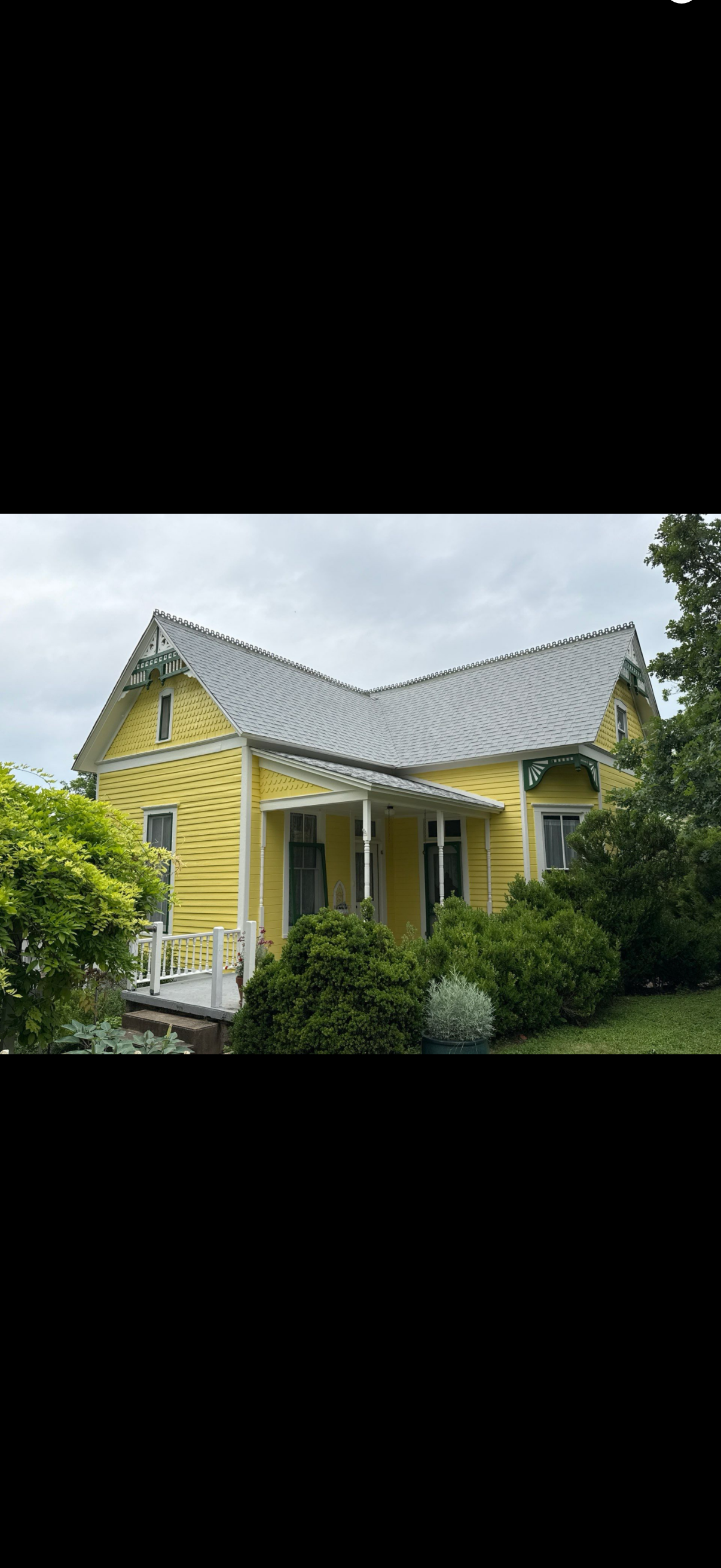 Yellow house with white trim and a front porch, surrounded by green shrubs and trees
