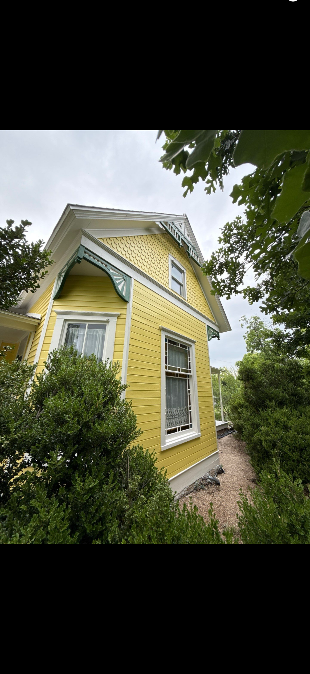 Yellow Victorian-style house with green trim, seen from below amid trees and bushes