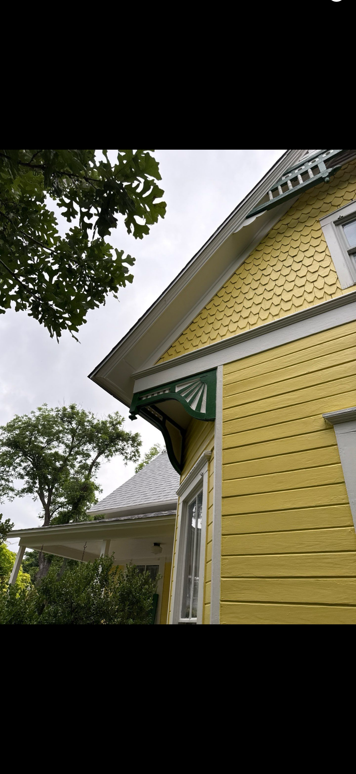 Yellow clapboard house with white trim and porch, viewed from below against an overcast sky.