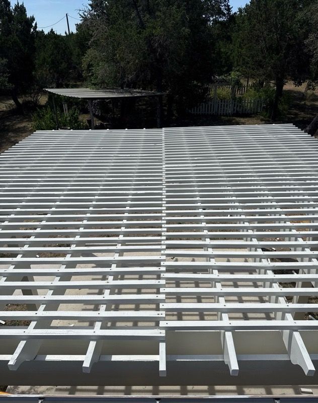 White metal roof framing under construction outdoors, with trees in the background.
