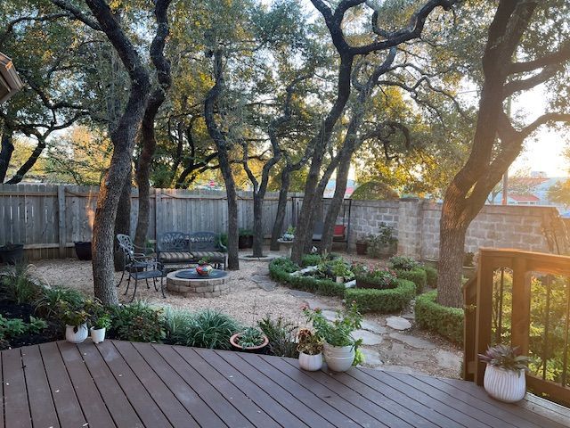Wooden deck overlooking a shaded backyard garden with trees, potted plants, and a stone path