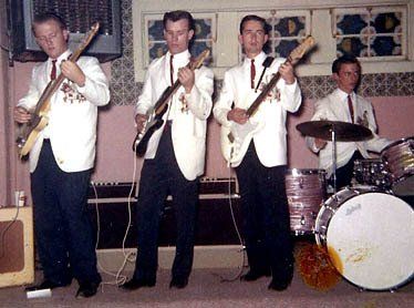 four men in white tops and black pants playing guitars