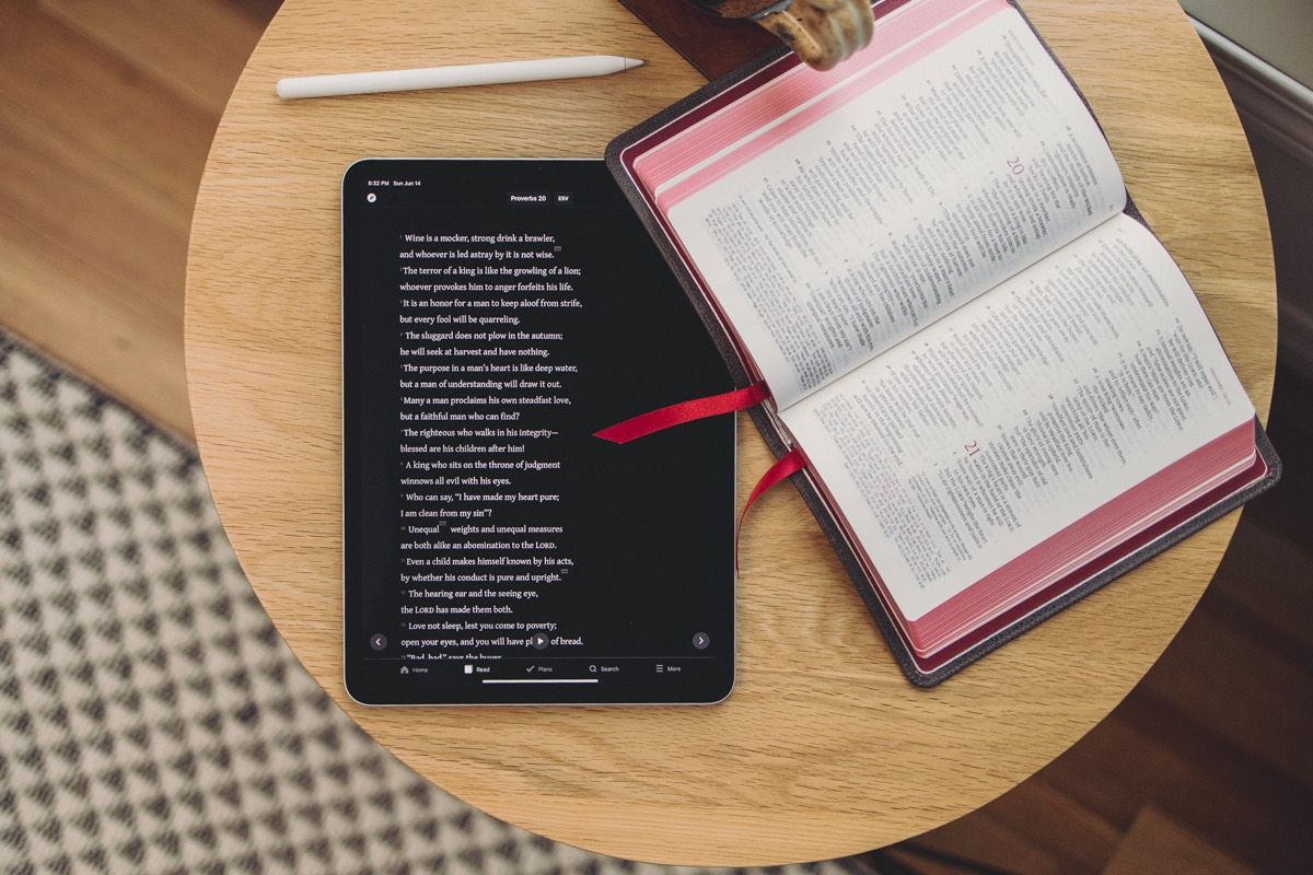 Tablet and open book on a wooden table, with a pen.