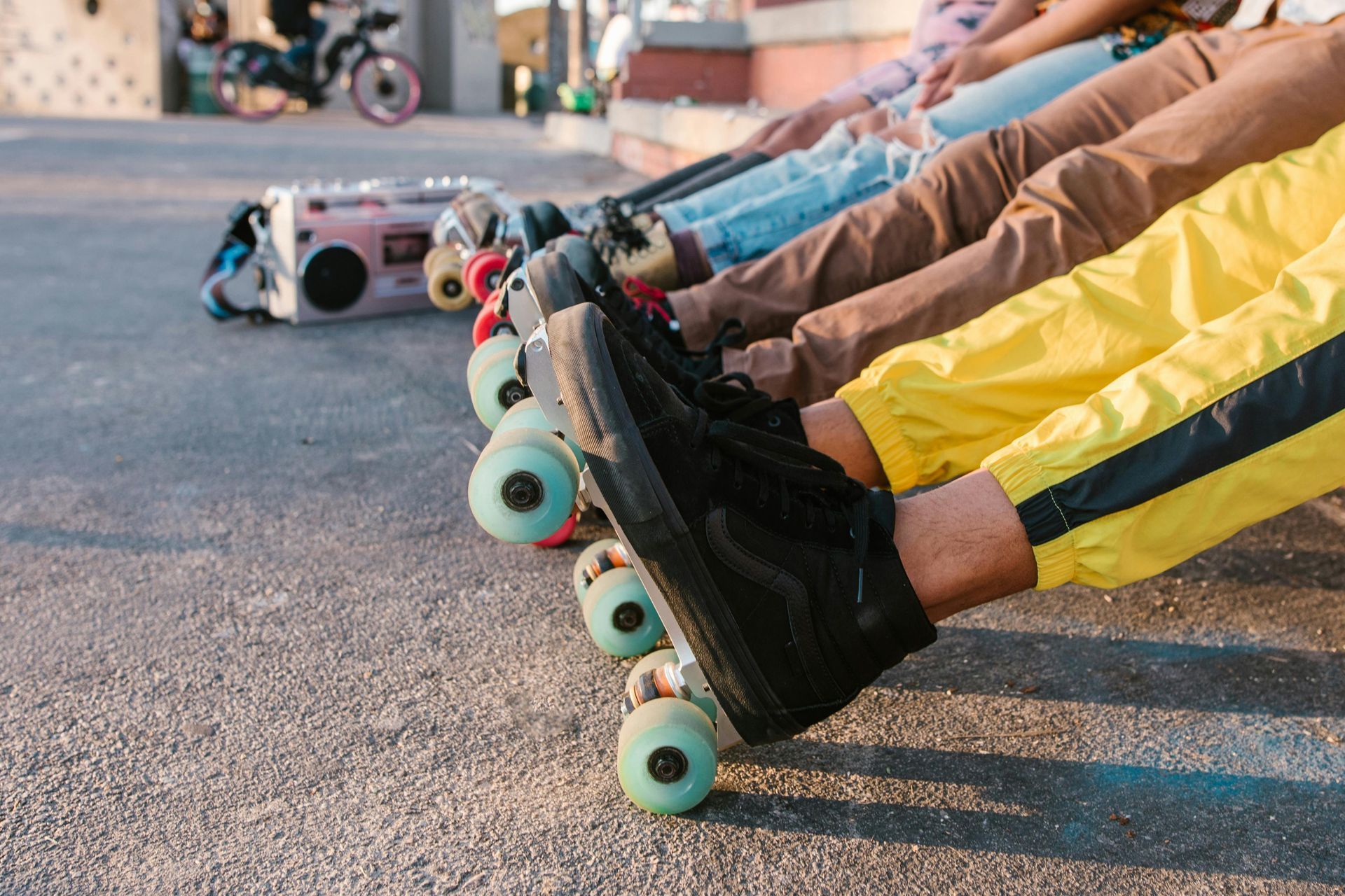 People with skateboards, wearing colorful pants, resting on concrete.