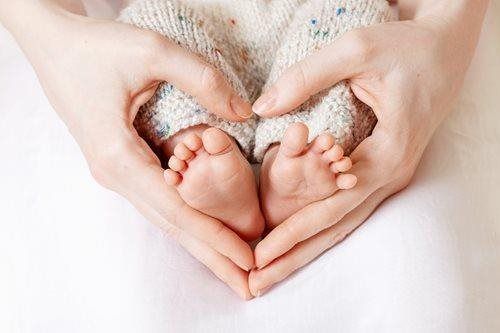Newborn baby's feet cradled in adult hands, forming a heart shape on a soft white blanket