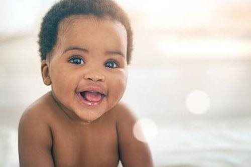 Smiling baby with curly hair, leaning forward on a soft white background