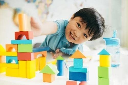 Child playing with colorful toy blocks at a table, smiling and reaching toward the stack
