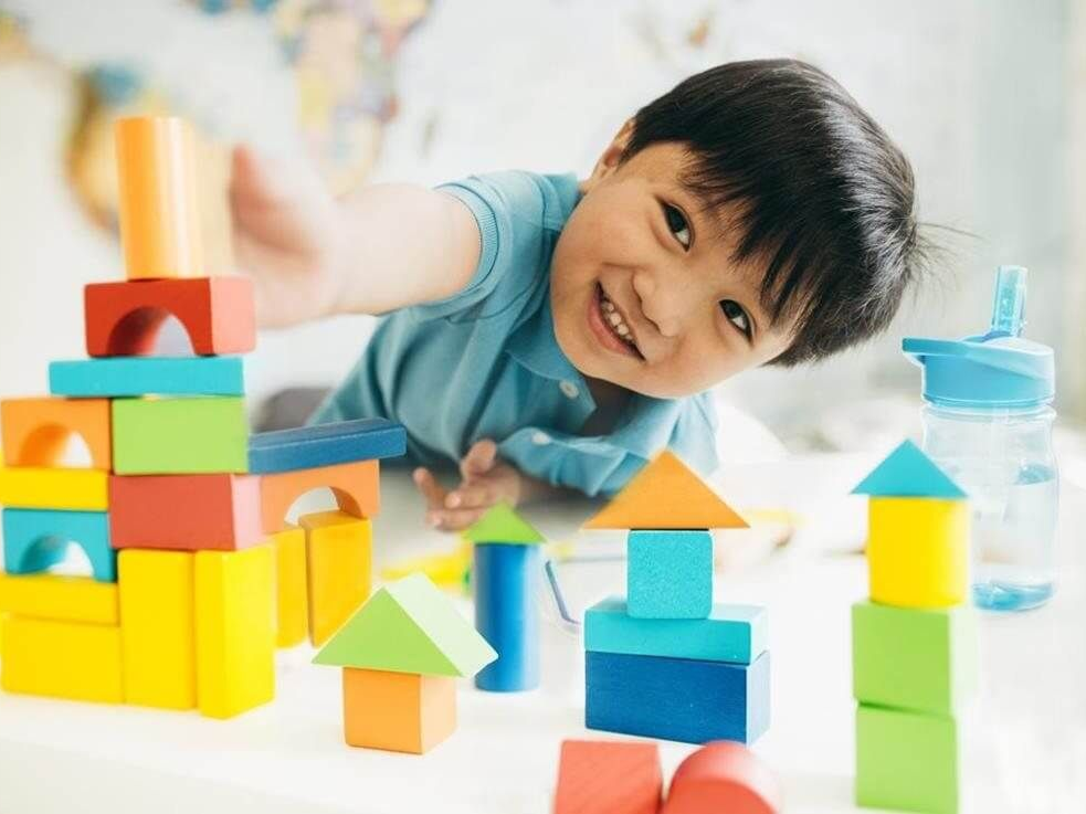 Child playing with colorful toy blocks at a table, smiling and reaching forward.