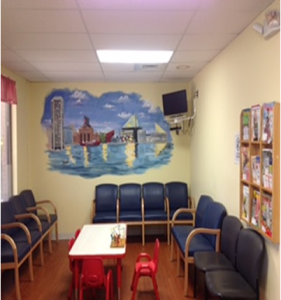 Waiting room with blue chairs, red table and stools, mural on the wall, and a small TV.