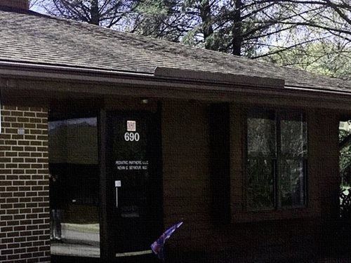 Brick office entrance with dark glass doors and windows, marked 690, beneath a tree-lined roofline
