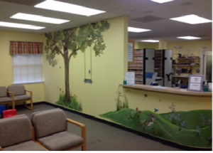 Bright waiting room with couches, reception desk, indoor tree mural, and fluorescent ceiling lights
