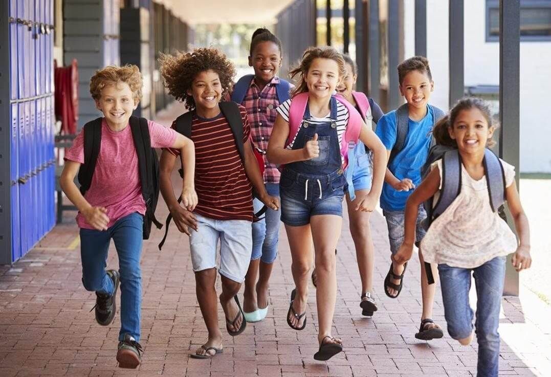 Five children with backpacks walking happily down a school hallway