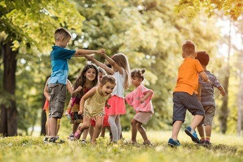 Children playing together in a sunlit park, dancing and holding hands under green trees