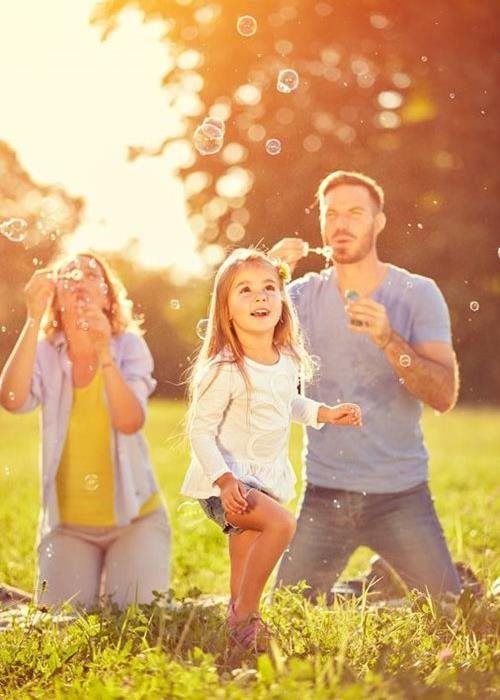 Family running through a sunny field, smiling and holding hands with bright sunlight behind them