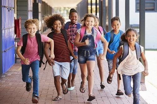 Children running and smiling down a school hallway with backpacks