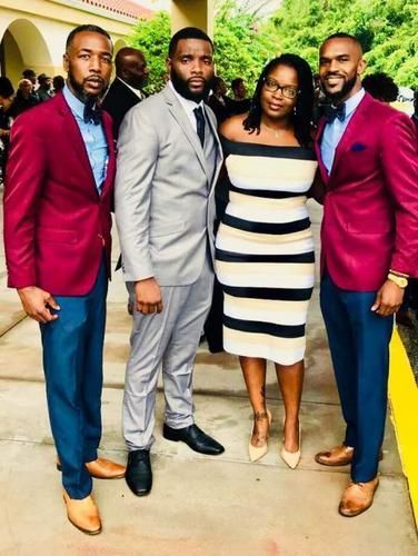 Four people posing together outdoors, wearing colorful formal outfits and smiling.