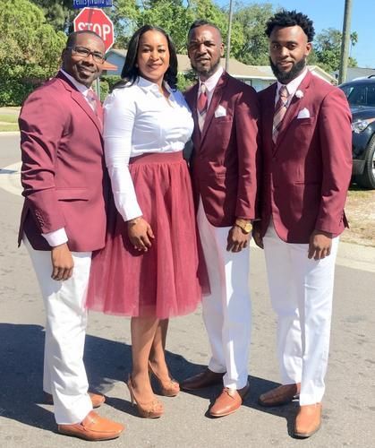 Four people posing outdoors in maroon and white coordinated outfits, standing in sunlight.
