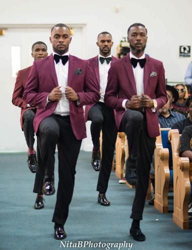 Men in maroon blazers and black bow ties walking down an aisle at a formal event
