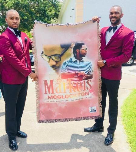 Two men in burgundy blazers holding a Maitres McGloeton event banner outdoors
