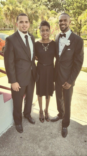 Three people dressed in black formalwear posing outdoors at a wedding or event.