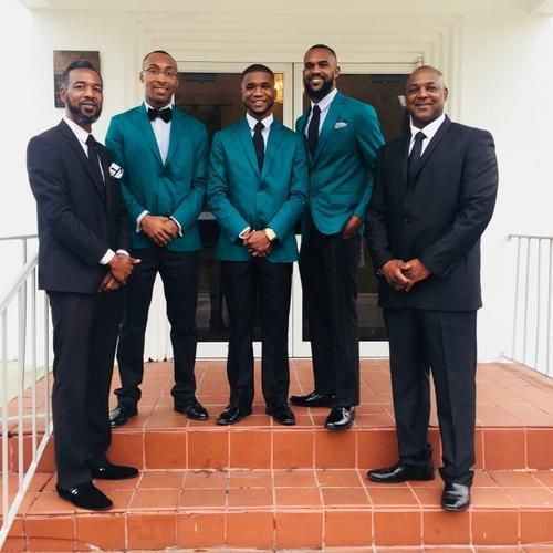 Five men in suits standing on a porch, three in teal jackets and two in black suits, posing together