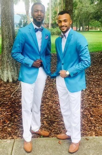 Two men in matching blue blazers and white pants posing outdoors in a park.