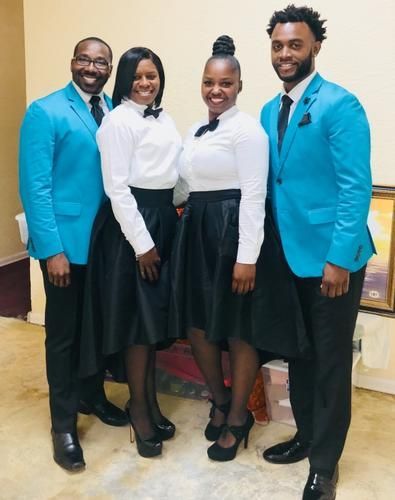 Four people posing indoors, two in bright blue blazers and two in white shirts with black skirts and pants.