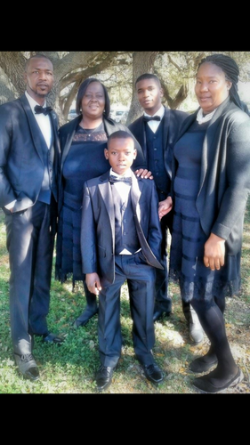 Five people in dark formal outfits posing outdoors on grass, with a young boy standing in front.
