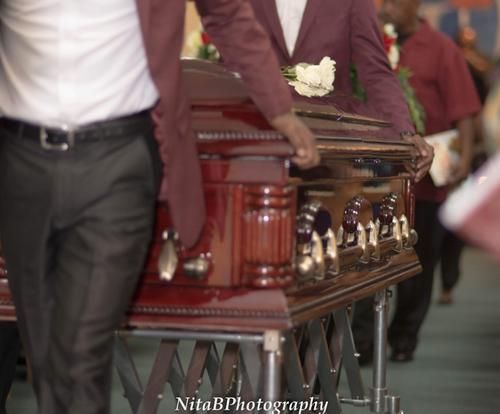 Men in maroon suits carrying a polished wooden casket at a funeral procession