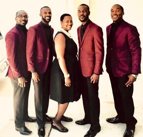 Five people in matching burgundy jackets and black outfits stand together in a studio, smiling.