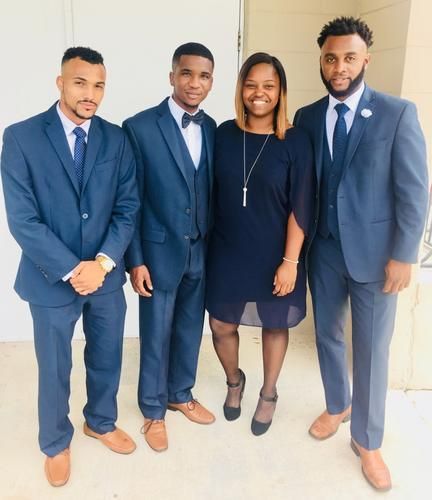 Four adults in coordinated navy outfits posing together indoors against a light wall.